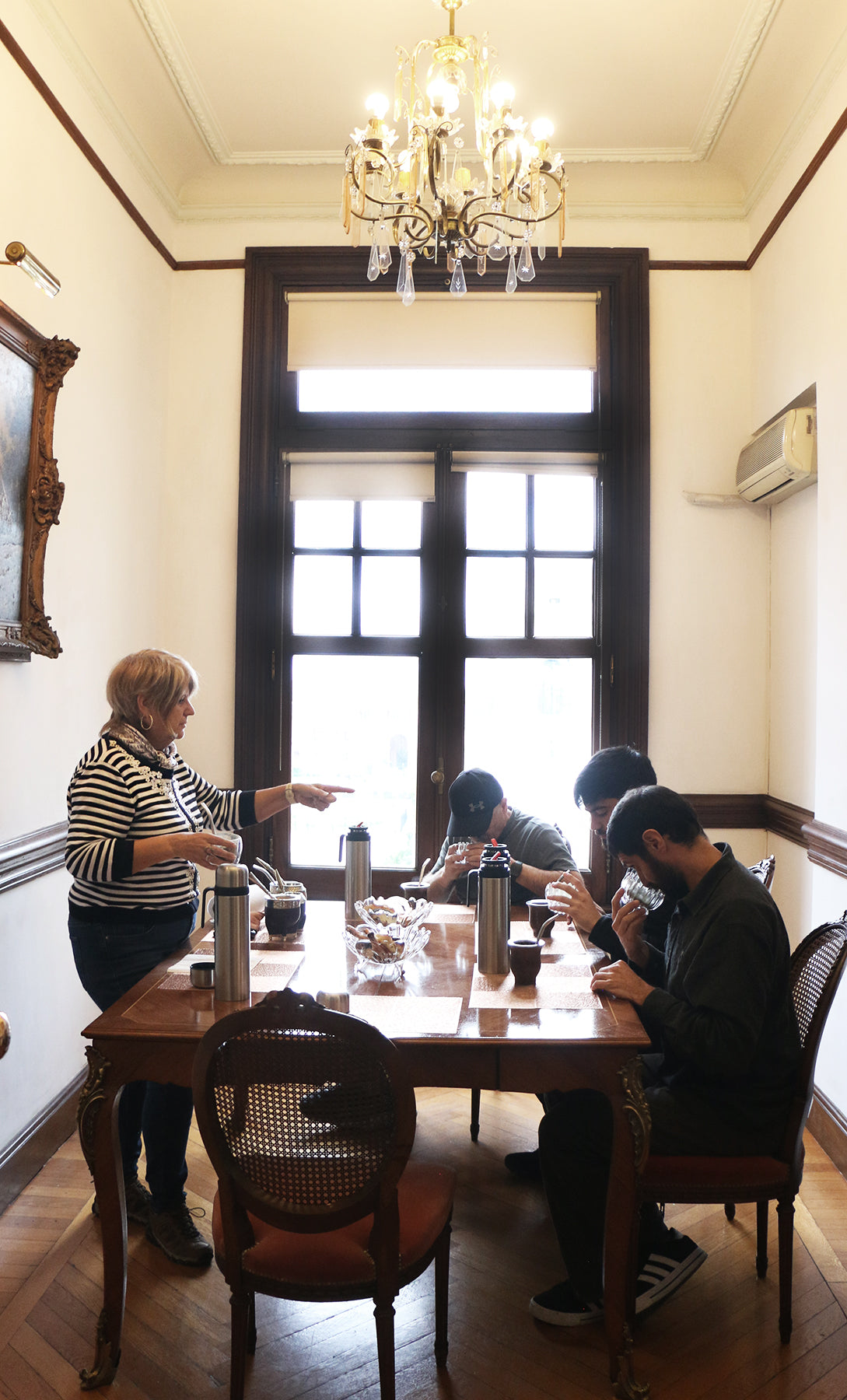 A group of people participating in a guided mate tasting session in a classic dining room with a chandelier