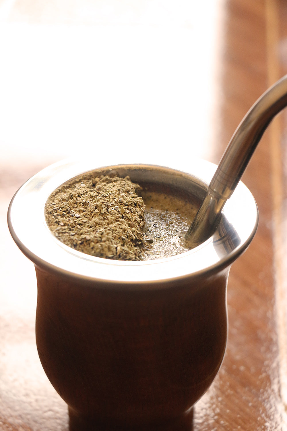 Close-up of a traditional mate cup with yerba mate and a metal bombilla straw, softly illuminated on a wooden surface