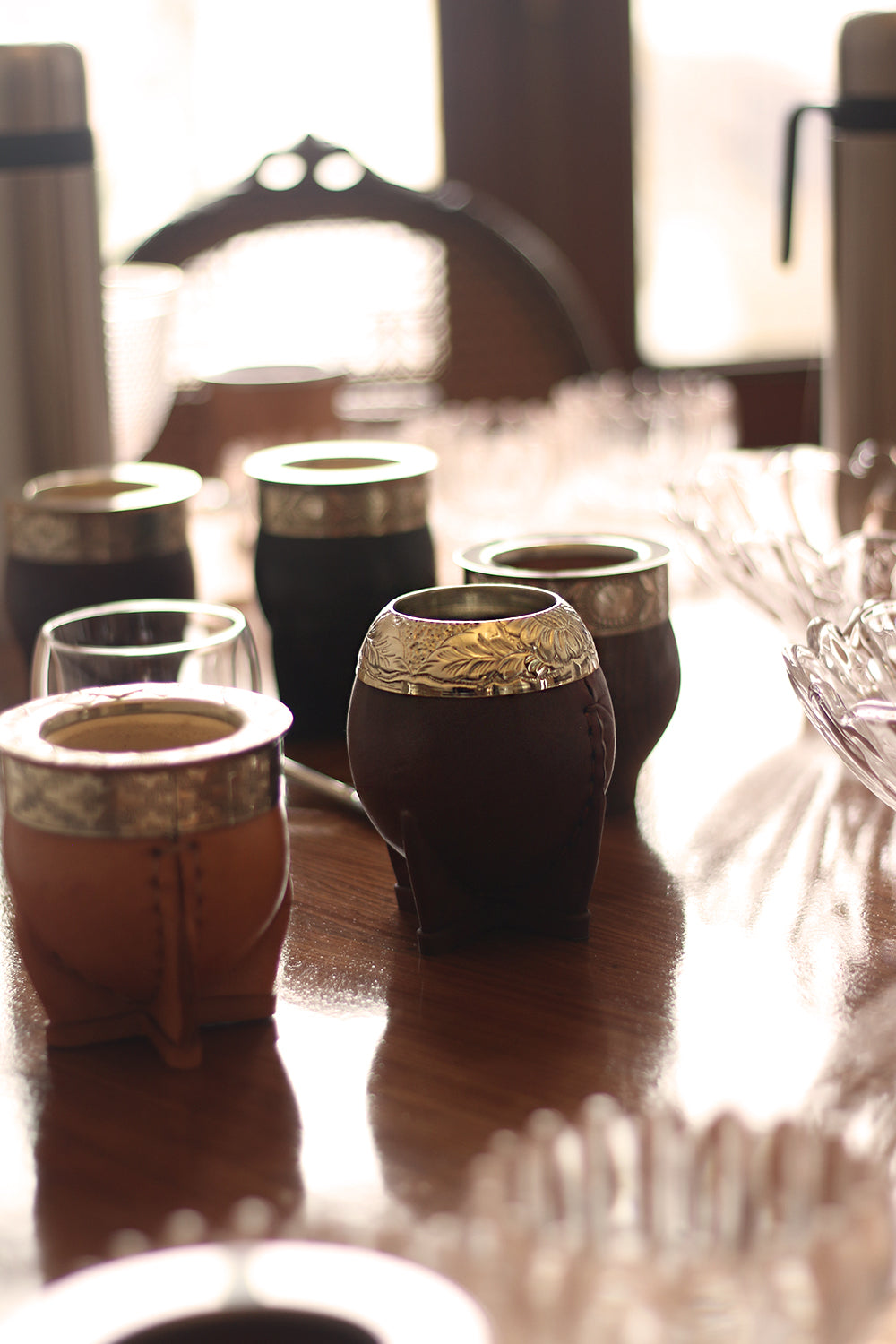 Close-up view of a collection of traditional leather-wrapped mate cups with silver rims, arranged on a wooden table