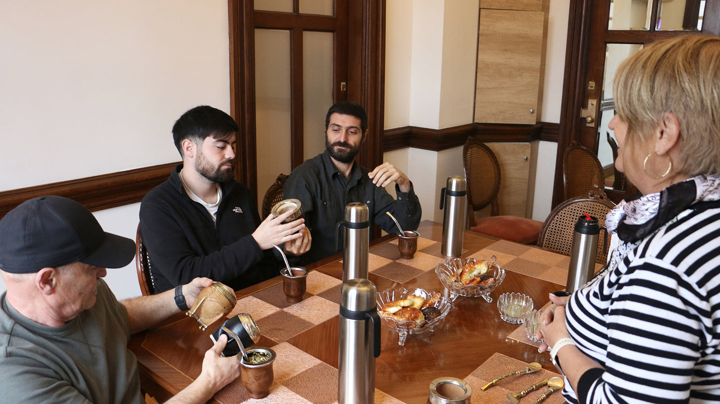 A group of people sharing a traditional mate tasting experience around a wooden table, examining various mate cups and accessories