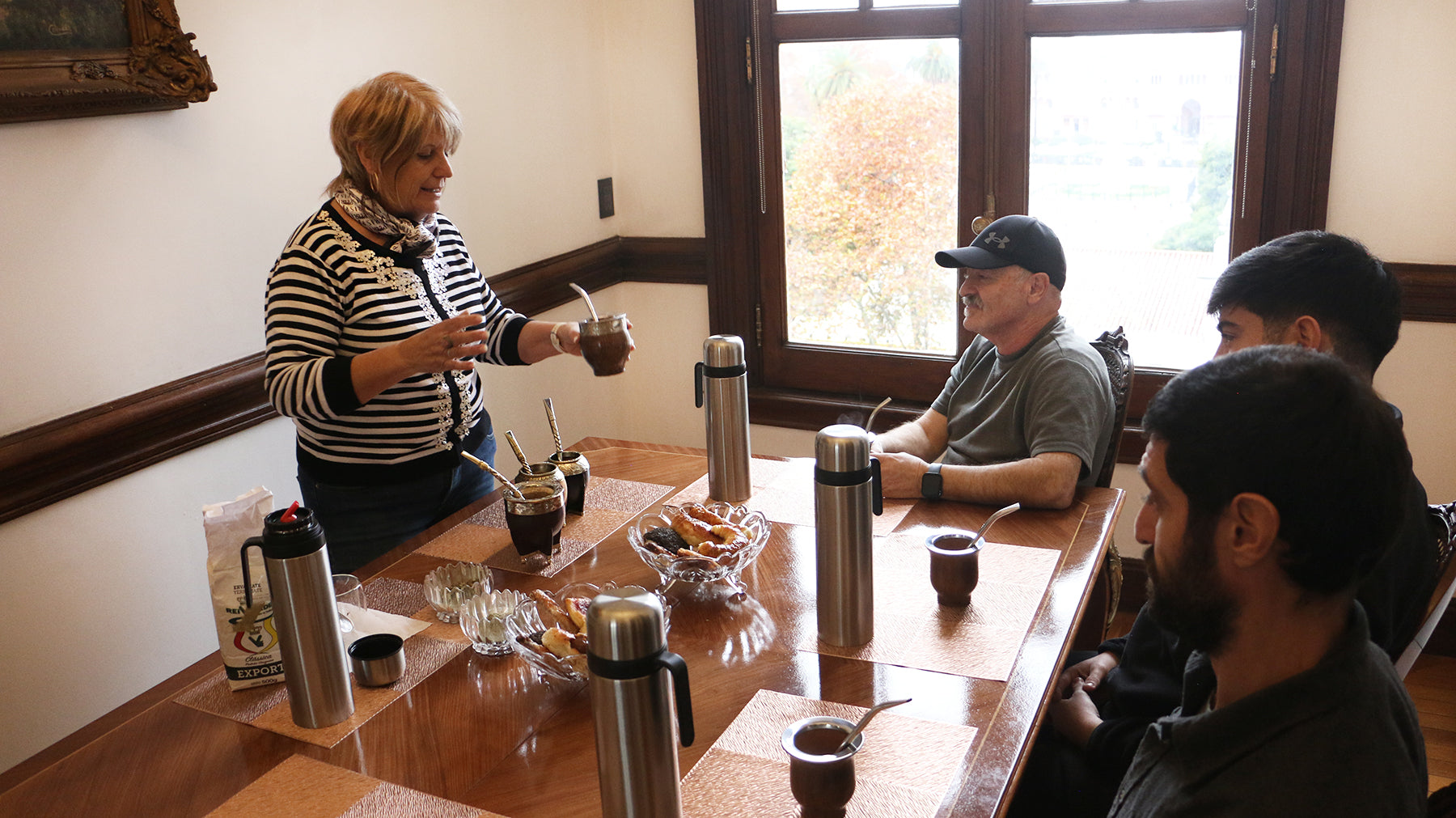 A group of people gathered around a wooden table for a traditional mate tasting, with thermoses and mate cups set out