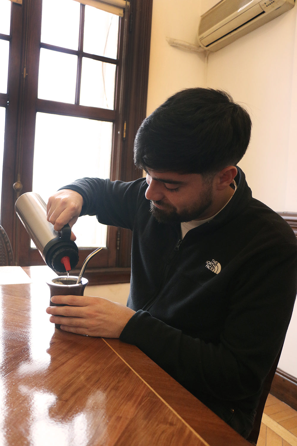 Young man pouring hot water from a thermos into a traditional mate cup, focusing on the preparation process