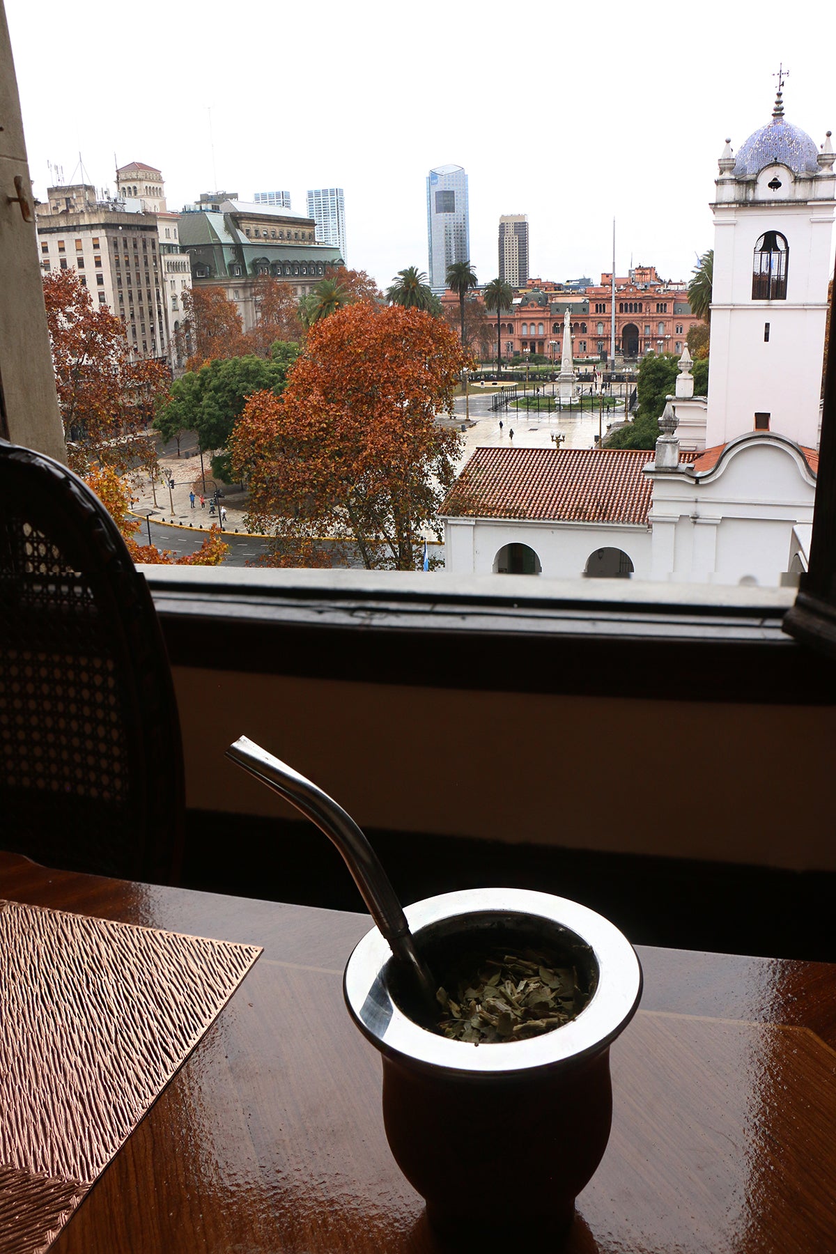 Traditional mate cup with a metal straw placed on a table, with a scenic view of Plaza de Mayo and the Buenos Aires cityscape in the background