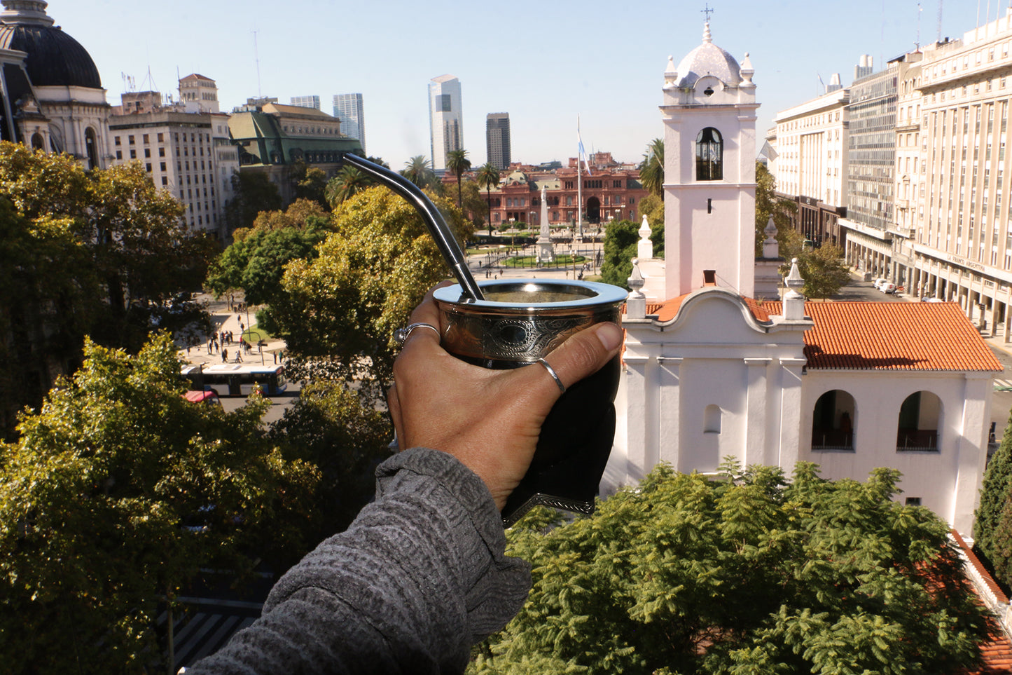 Person holding a traditional mate with a straw, overlooking Plaza de Mayo and the Metropolitan Cathedral in Buenos Aires in Materba Mates mate tasting showroom