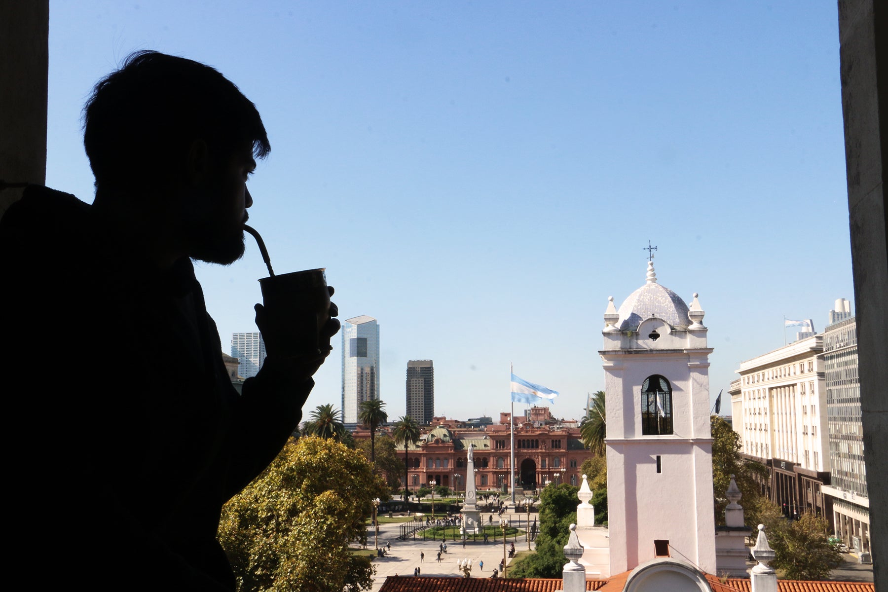 Silhouette of a person drinking traditional yerba mate with a straw, overlooking Plaza de Mayo and Cabildo in Buenos Aires