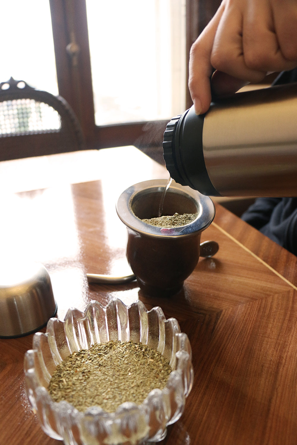 Close-up of hot water being poured from a stainless steel thermos into a traditional mate cup filled with yerba mate
