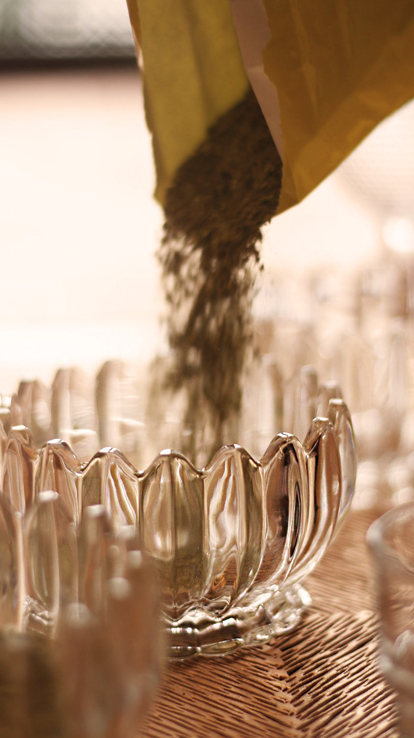 Dry yerba mate being poured from a bag into a glass bowl for a tasting session